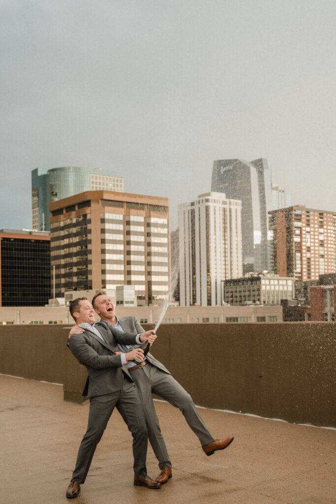 couple popping champagne for their engagement photos on a rooftop