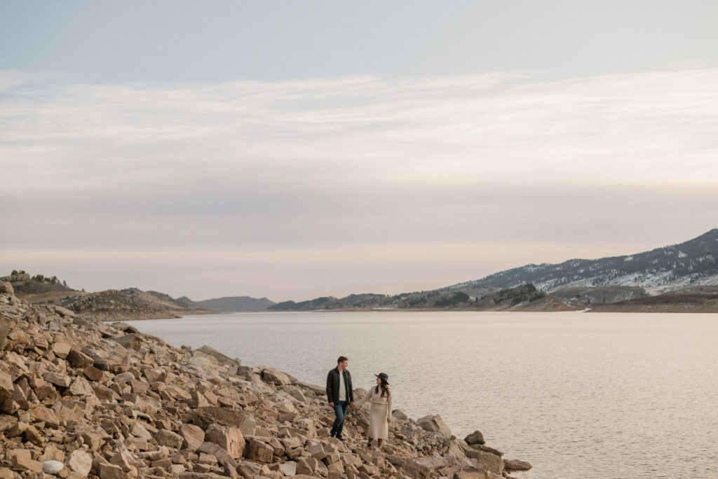 couple walking on a rocky shore in front of a lake for their engagement pictures
